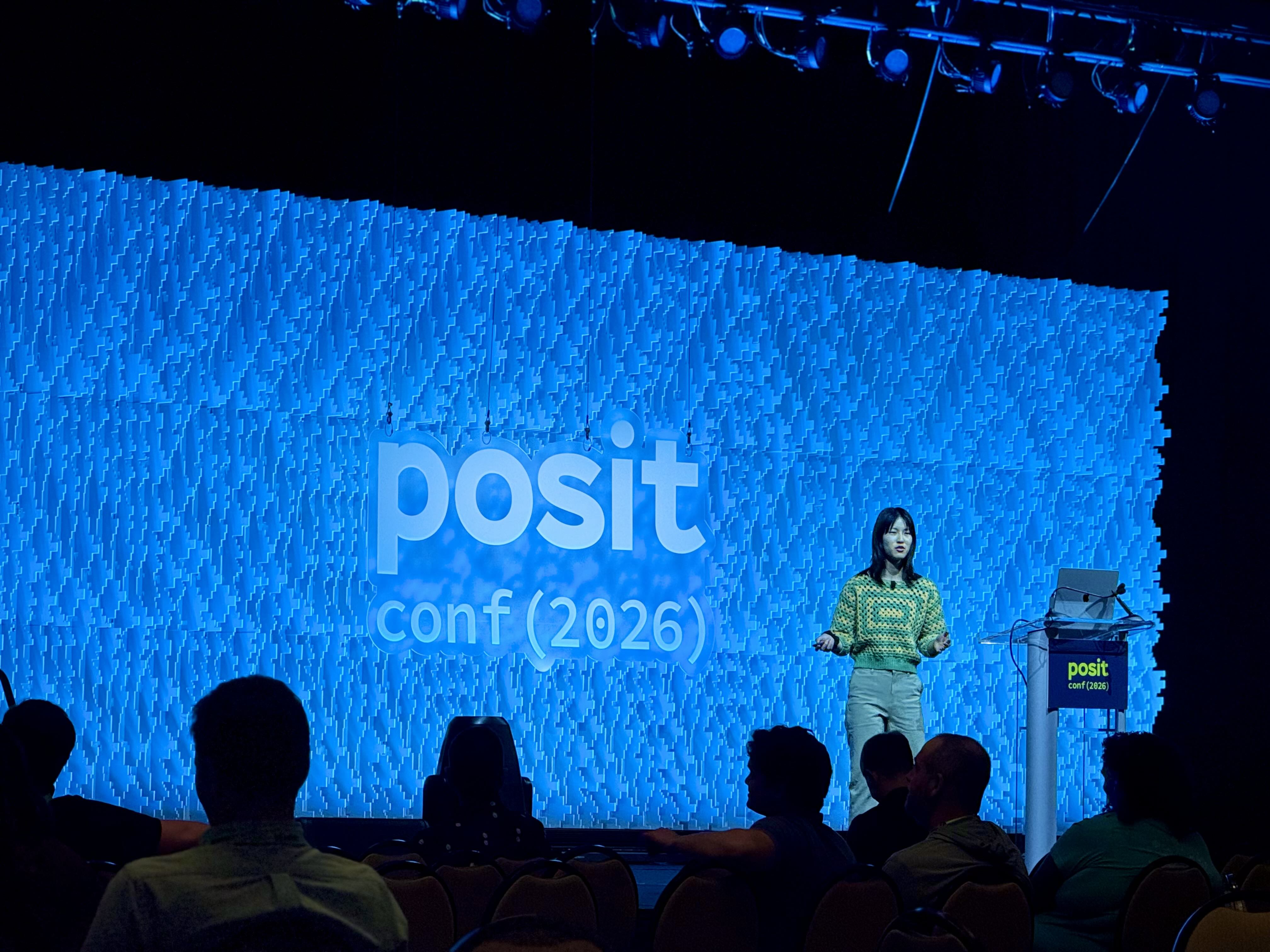 Sharon on stage at posit conf 2026, giving this talk. She is wearing a green and yellow crocheted cropped sweater.